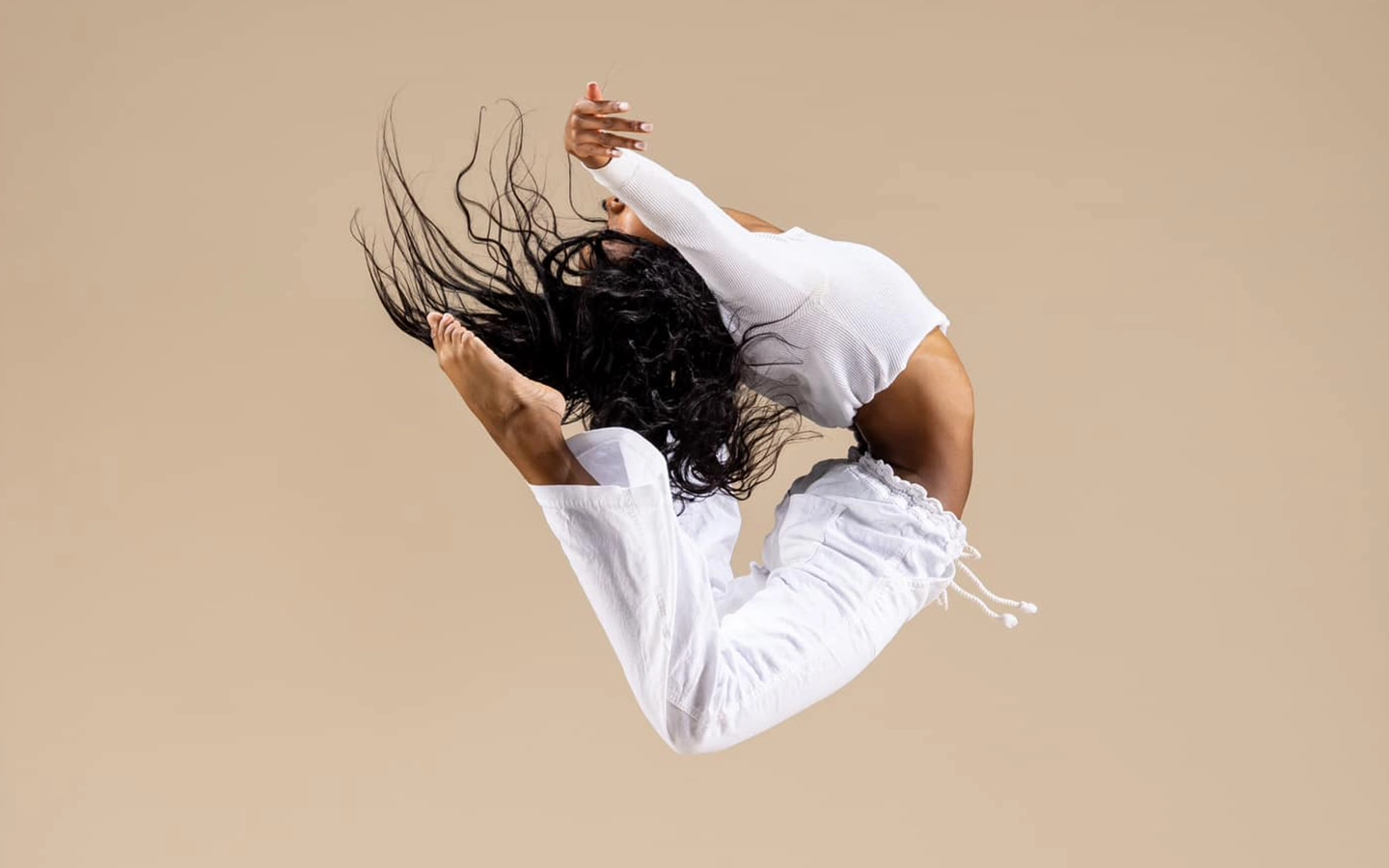 Dancer jumping in the air in a dramatic pose on tan background